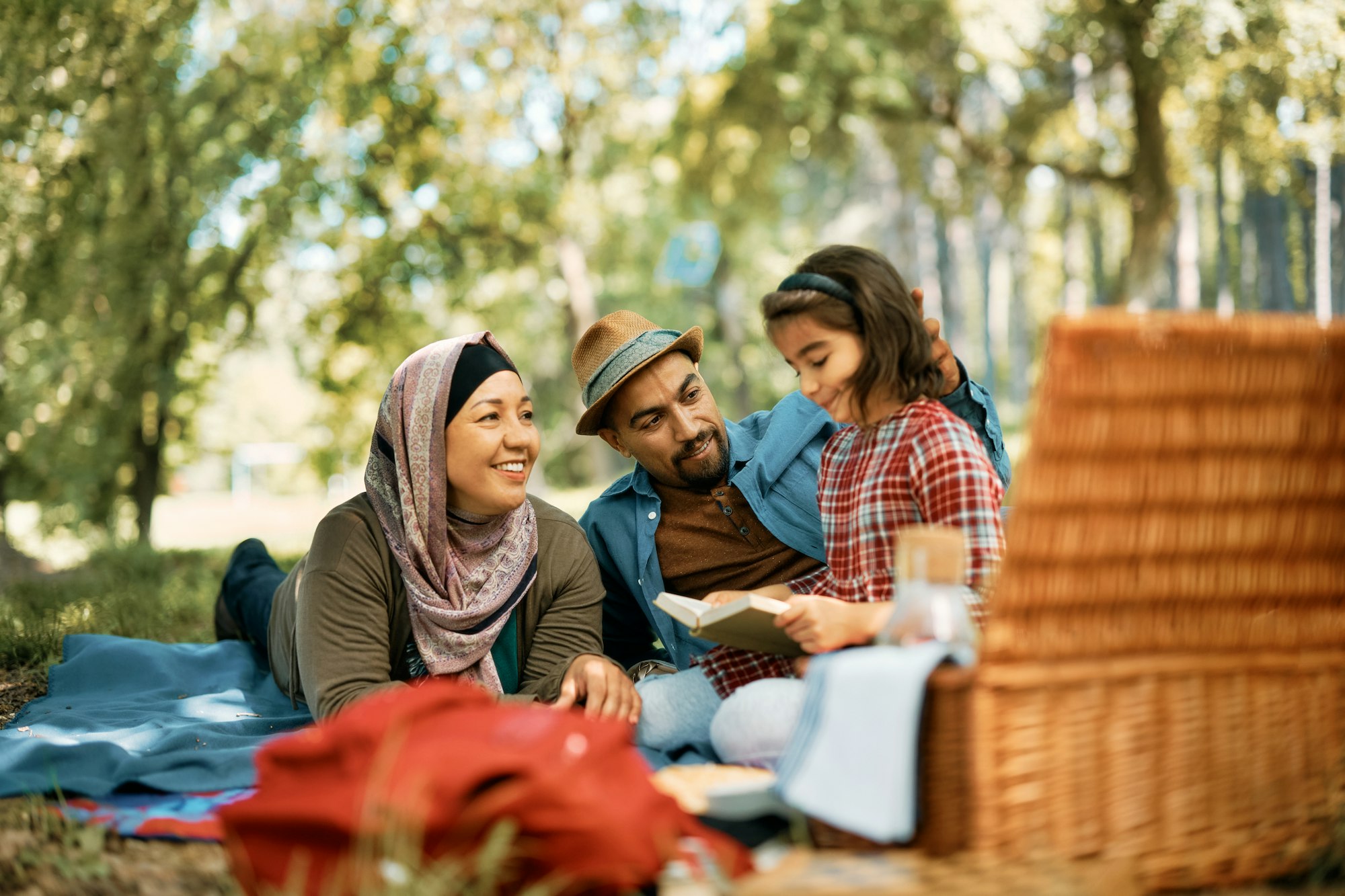 Happy Muslim family reading a book on picnic in nature.